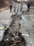 men walk down cracked highway with billowing smoke