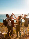 Young adult friends on a hike celebrate reaching a summit near the coast, full length, side view