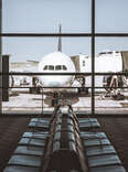 A mostly empty airport terminal, with windows showing a passenger airplane on the runway. 