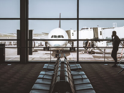 A mostly empty airport terminal, with windows showing a passenger airplane on the runway.