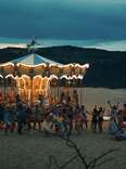 A birghtly lit carousel set up on the dark beach. 