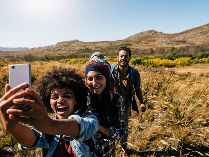Group of friends taking selfie on country hike. Young people hiking in countryside and taking pictures with smart phone.