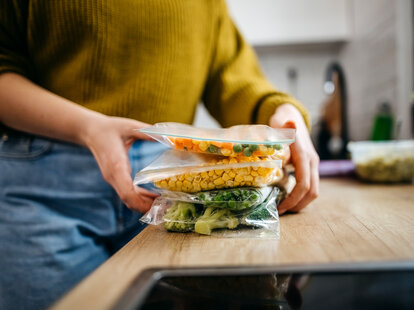 Young woman packing up leftover food in ziploc bags.