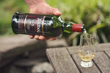 hand pouring bottle of ardbeg scotch whiskey