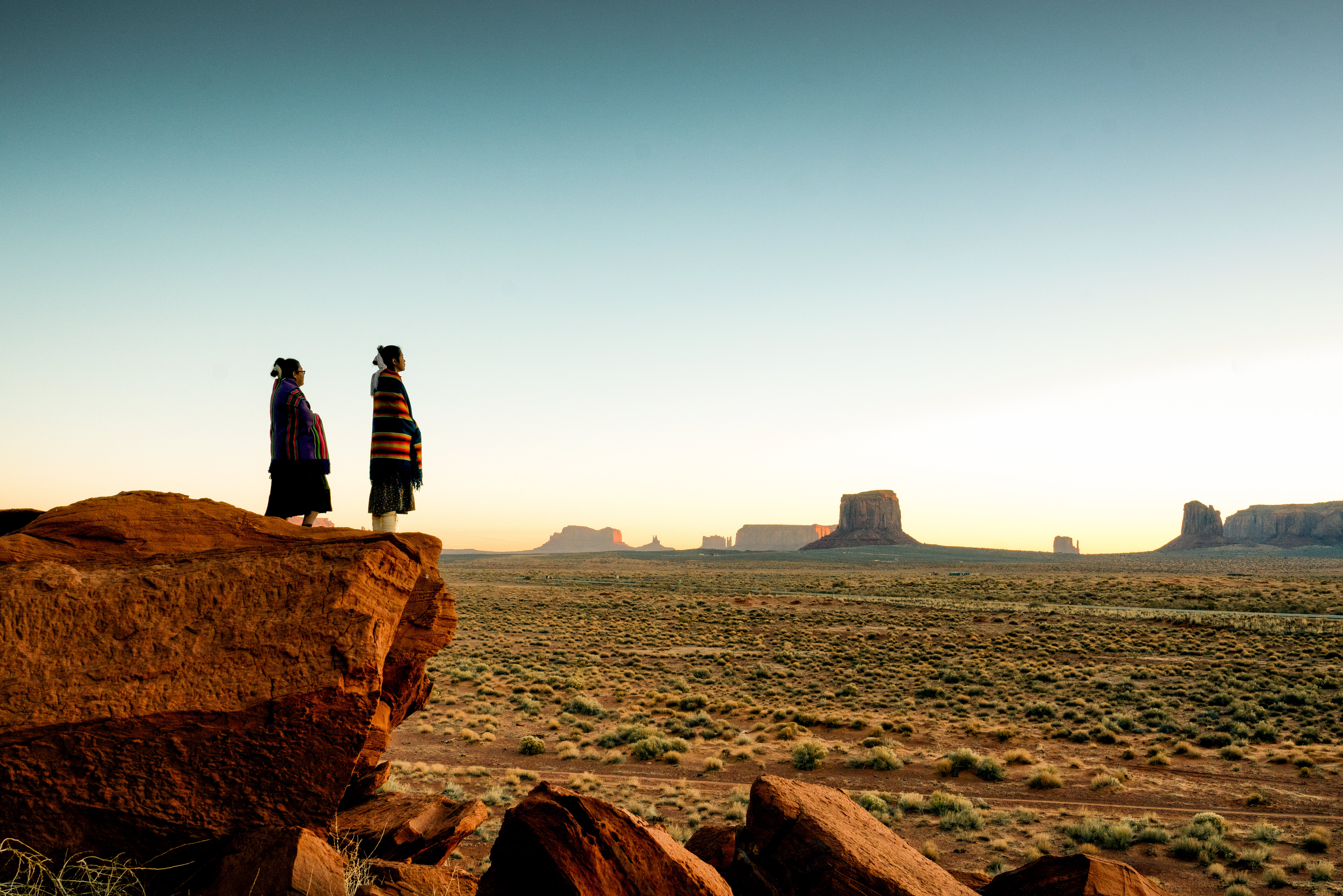 Navajo girls wrapped in handwoven traditional blankets enjoying a grand sunrise or sunset in Monument Valley