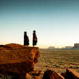 Navajo girls wrapped in handwoven traditional blankets enjoying a grand sunrise or sunset in Monument Valley