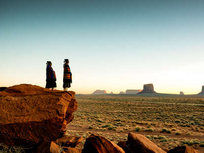 Navajo girls wrapped in handwoven traditional blankets enjoying a grand sunrise or sunset in Monument Valley