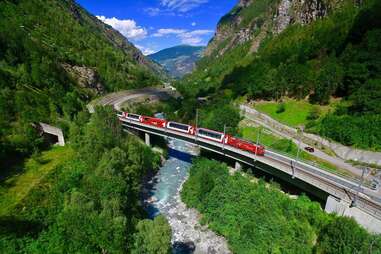 glacier express train, rolling through verdant green hills over a river