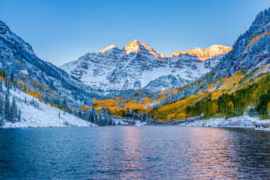 snowy peaks of maroon bells surrounding lake at sunrise