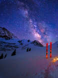 a glowing tent under the milky way with skis stuck in the snow outside of it