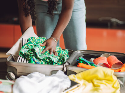 woman stacking clothes and shoes into bag case, trying to pack hand luggage