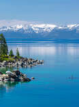 person paddle-boarding on crystal blue waters surround by snow-capped mountains