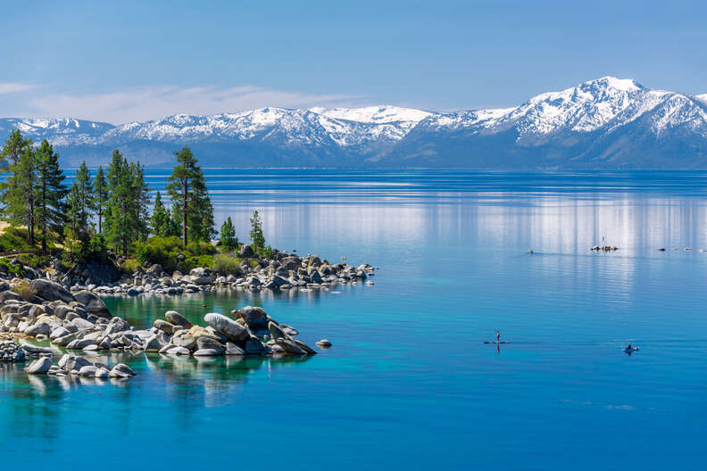 person paddle-boarding on crystal blue waters surround by snow-capped mountains