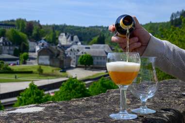 person pouring a blonde ale with old town Bouillon, Belgium in the background