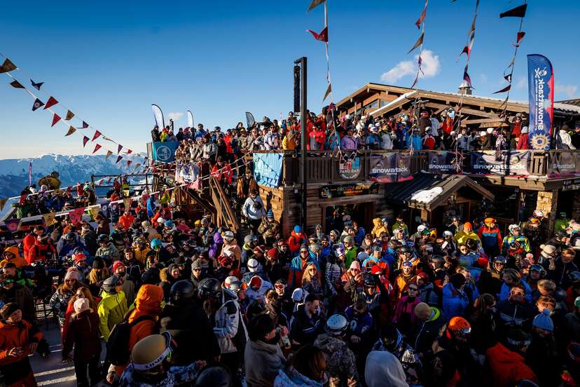 people in snow gear outdoors around a wooden chalet 