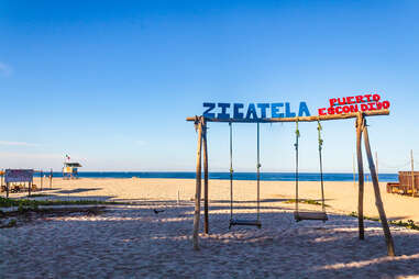 swings on the beach with sign that reads "zicatela"
