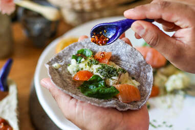 close up of hands pouring salsa over taco