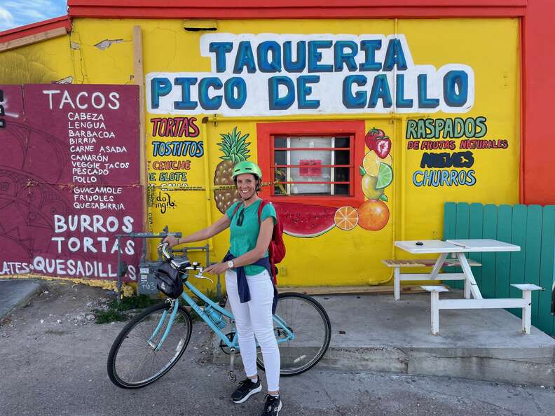 woman holding a bicycle standing in front of taqueria pico de gallo