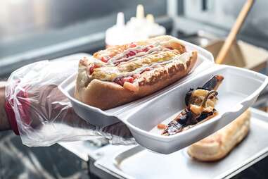 a sonoran hotdog in a styrofoam container being held out for the camera