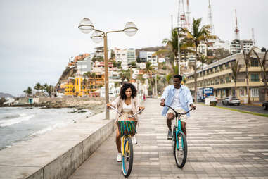 couple riding bikes down a boardwalk in coastal mexico