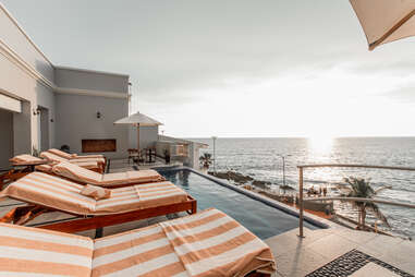 three chaise lounges facing a pool and the open water in mexico