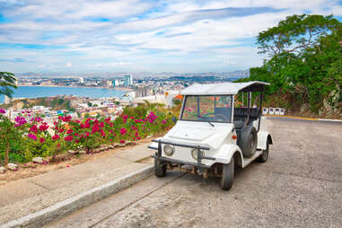 a white taxi in front of a panoramic view of mazatlan mexico