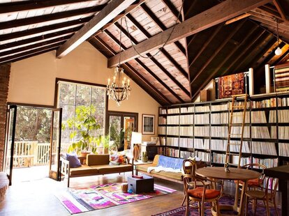 A spacious room with a well decorated floor to ceiling bookshelf and a view of a beautiful landscape outside the windows.