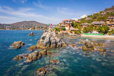 The Mexican flag sits on top of a large rock in a shallow area of Playa la Ropa, Zihuatanejo