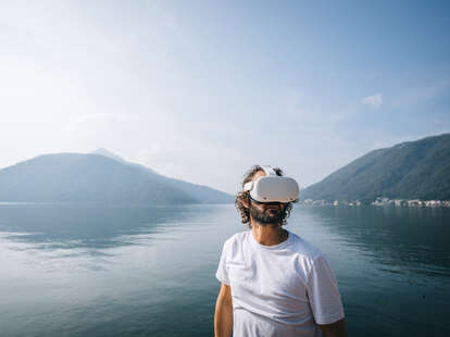 Man wears VR glasses by a lakeshore on a sunny autumnal morning