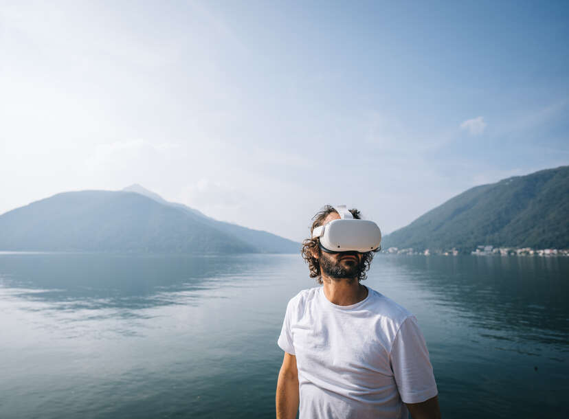 Man wears VR glasses by a lakeshore on a sunny autumnal morning