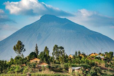 a rwandan village dwarfed by a massive volcanic mountain in the background