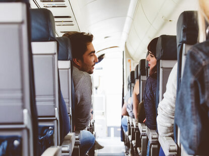 Interior of airplane with couple sitting in aisle seats and talking.