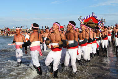 topless men in white pants carrying a shrine 