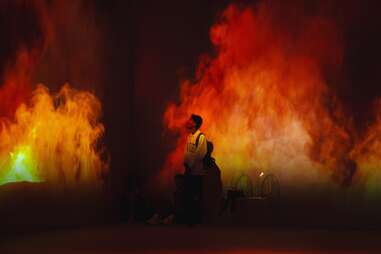 a man standing in a room with flames projected on the walls around him as part of an immersive installation