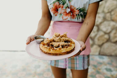 a woman holds a plate of chicken and waffles