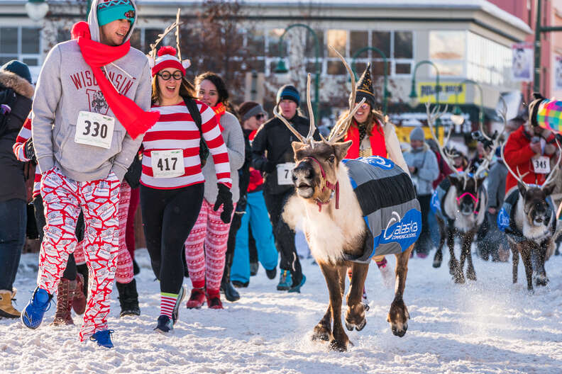 a reindeer runs on snow, followed by humans in costume