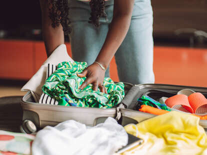 Woman stacking clothes and shoes into bag case, trying to pack hand luggage
