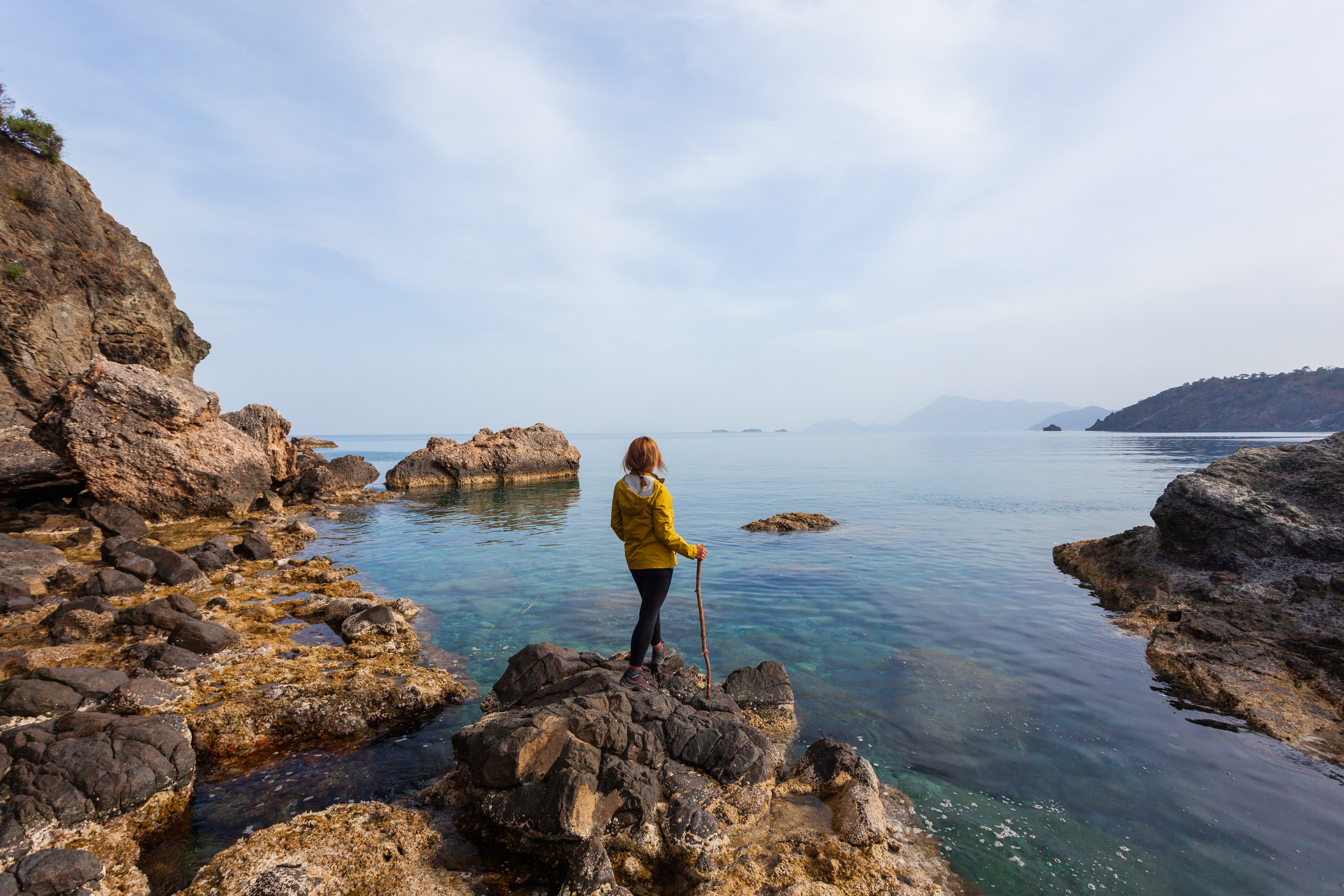 A woman is standing on the rocky shore, watching the sea view