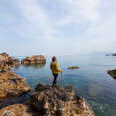 A woman is standing on the rocky shore, watching the sea view