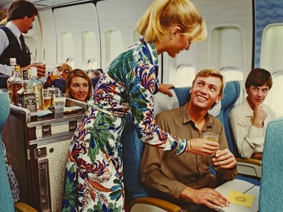 archival photo of flight attendant serving a ginger ale to an airplane passenger who is smiling