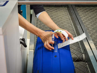 A check-in gate employee attaches a luggage tag to suitcase of passenger with a closeup of hands.