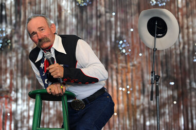 a man in Western attire performs on stage with his cowboy hat hung on the microphone stand.