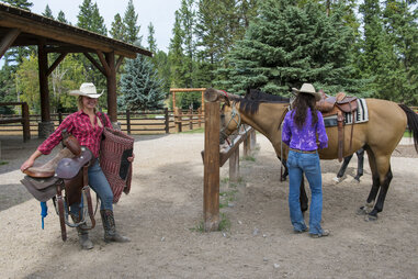 two women in cowboy attire saddling up a horse