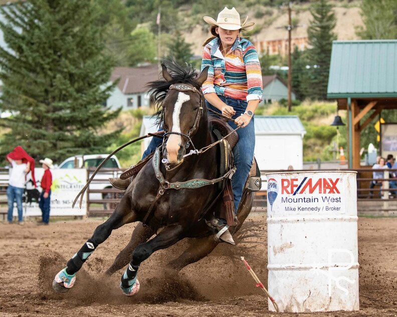 a cowgirl on a horse riding around a barrel in a barrel racing event