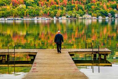 person standing on doc in the finger lakes surrounded by fall foliage