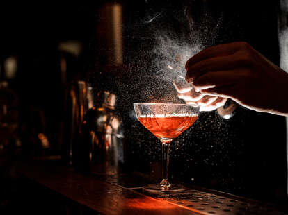 Barperson's hands sprinkling the juice into the cocktail glass