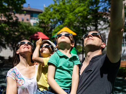 A family looks at the solar eclipse in the city street in a public park
