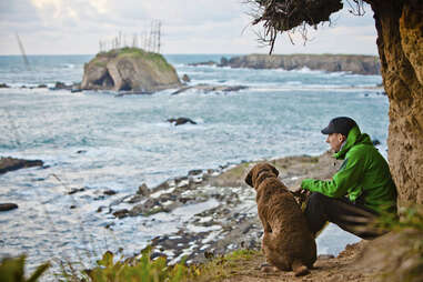 A young man sits with his dog near Sunset Bay on the Oregon Coast