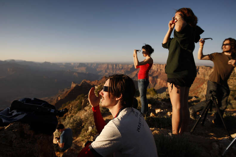 People protect their eyes with eclipse glasses while watching an annnular solar eclipse reaches in the Grand Canyon