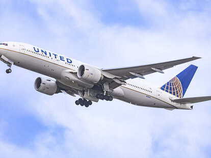 United Airlines Boeing wide body 777-200 aircraft as seen during take off and flying phase, passing in front of the air traffic control tower.